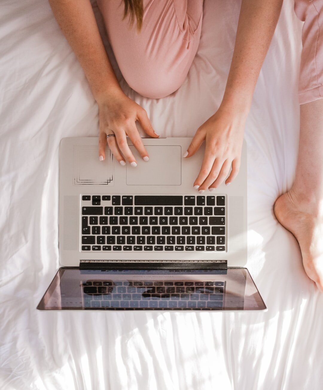 photo of person sitting on bed with silver laptop